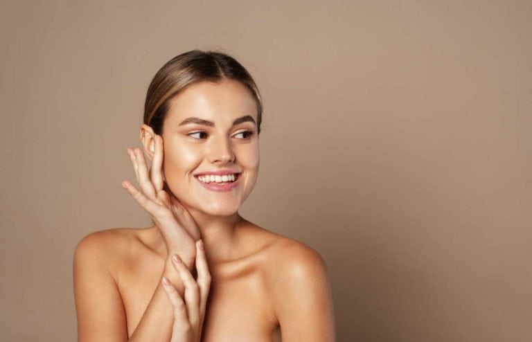 Mujer sonriendo con maquillaje natural y piel radiante en fondo beige.