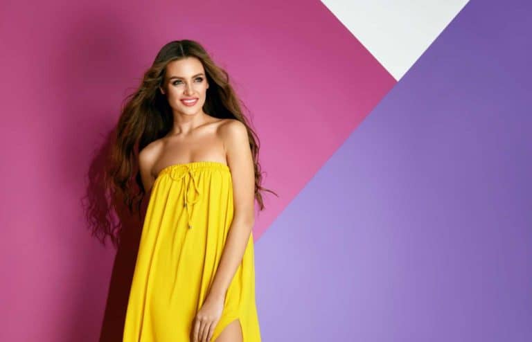 Mujer con maquillaje colorido y vestido amarillo en fondo rosa y morado.