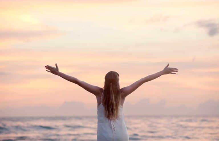 Mujer en la playa disfrutando del atardecer con los brazos abiertos.