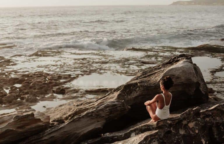 Mujer practicando yoga en la playa al atardecer para bienestar y autocuidado.