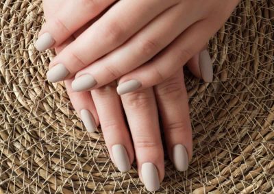 Uñas con esmalte Shellac en tono nude en manos femeninas sobre cesta de mimbre.